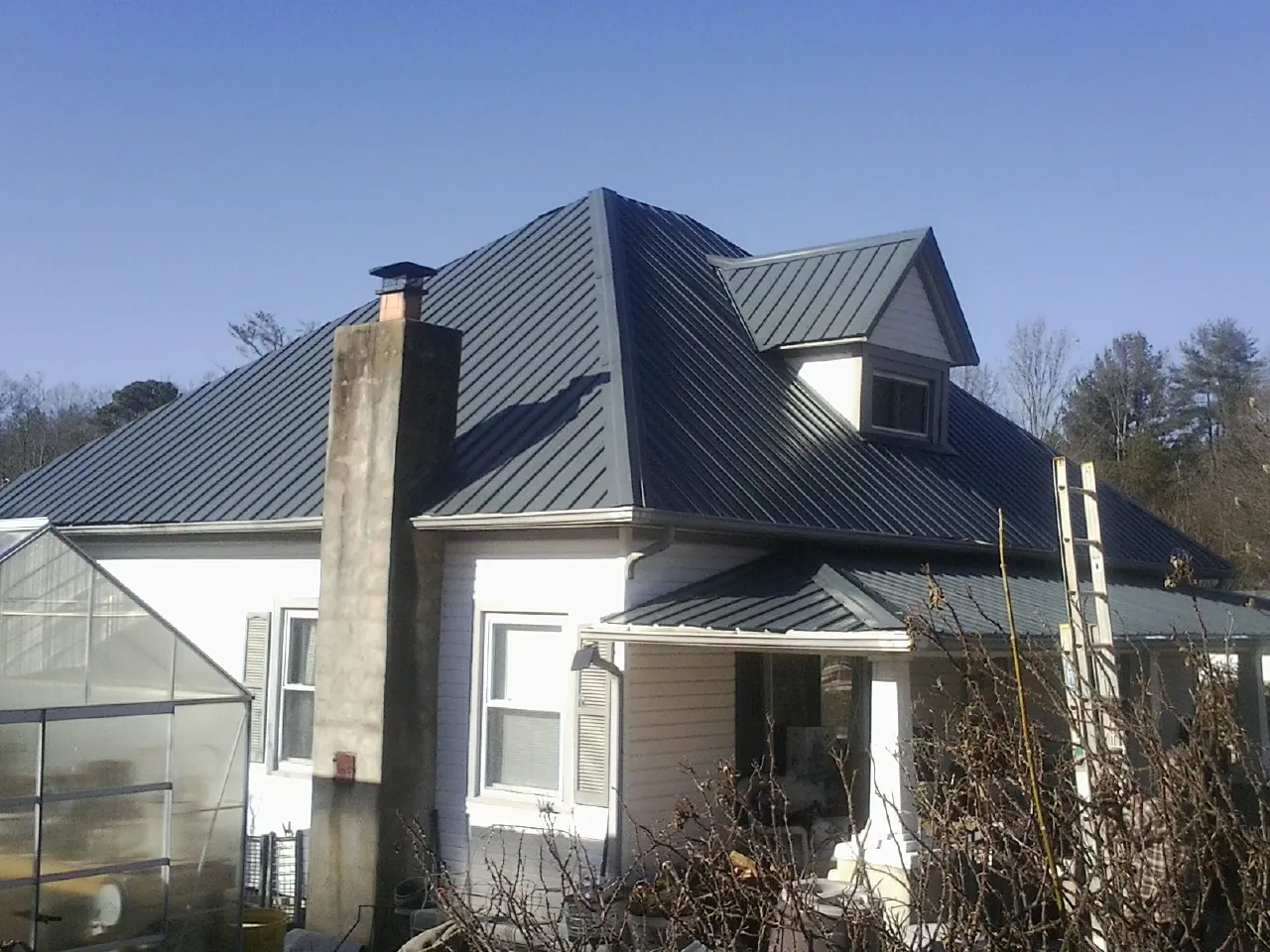 Dark blue standing seam metal roof on a white farmhouse with dormer — Slate & Tile Roof Repair by Roofing Brothers in Boykins