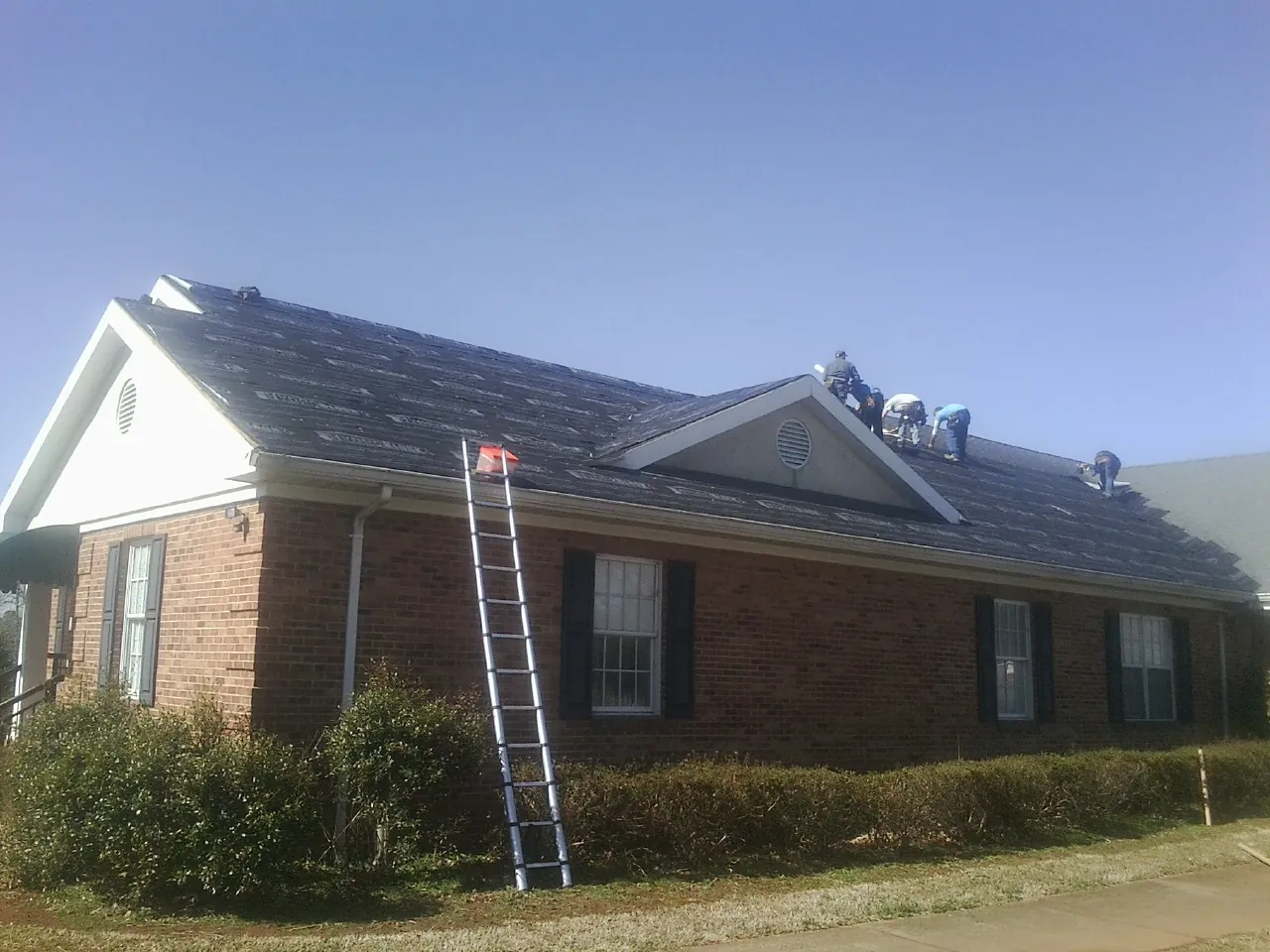 Crew tearing shingles off a brick ranch roof with a ladder set — Metal Roof Repair work by our crew in Boykins