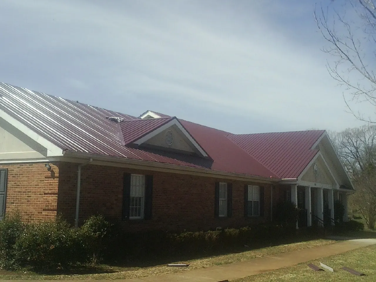 Red metal roof with gabled entries on a long brick building, from a Hail Damage Roof Repair job in Boykins