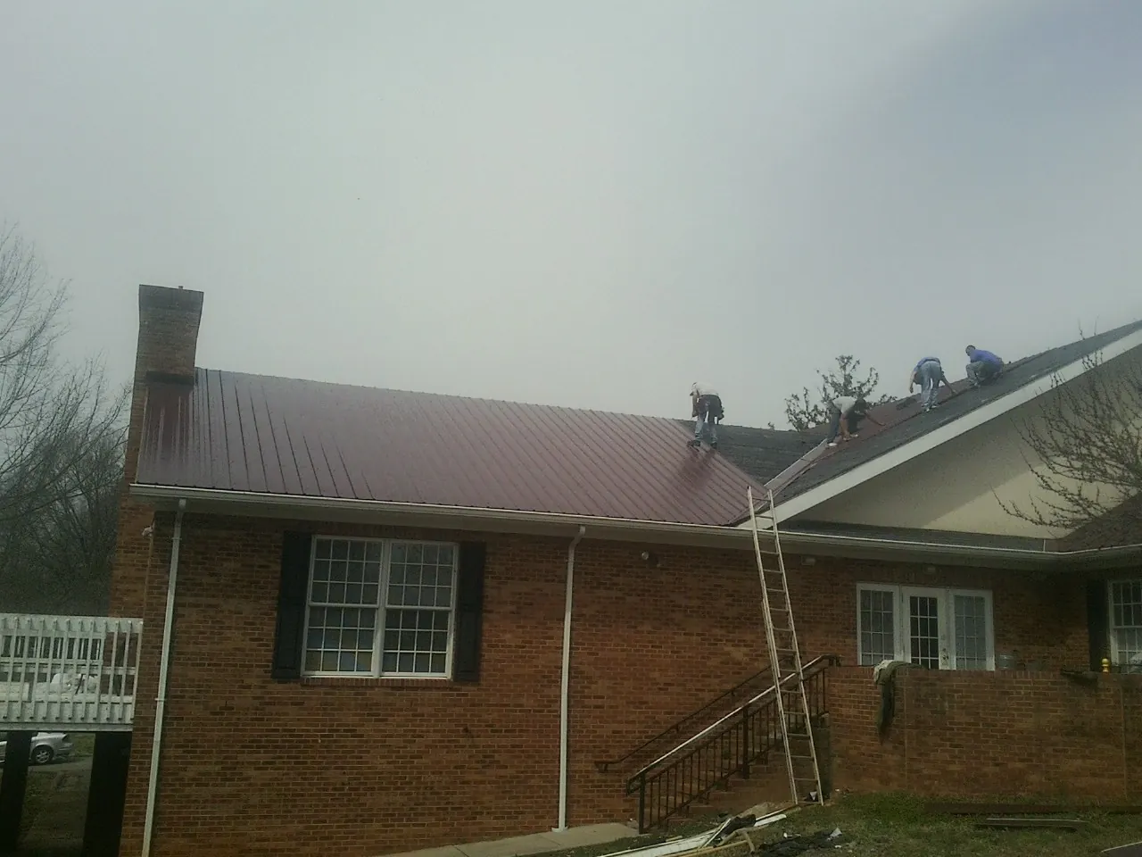 Crew setting red metal roofing panels on a brick home in Boykins