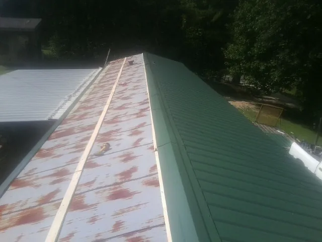 Old rusted panels beside newly installed green metal roofing — Wind Damage Roof Repair by Roofing Brothers in Boykins