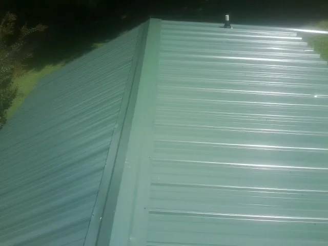 New green metal panels meeting at the ridge of a roof — Flat Roof Repair work by our crew in Boykins