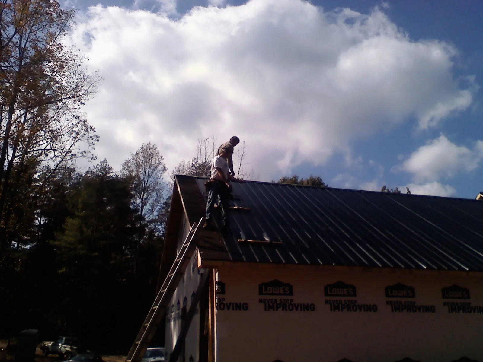 Roofer fastening dark metal panels high against a cloudy sky, from a Roof Inspection job in Boykins
