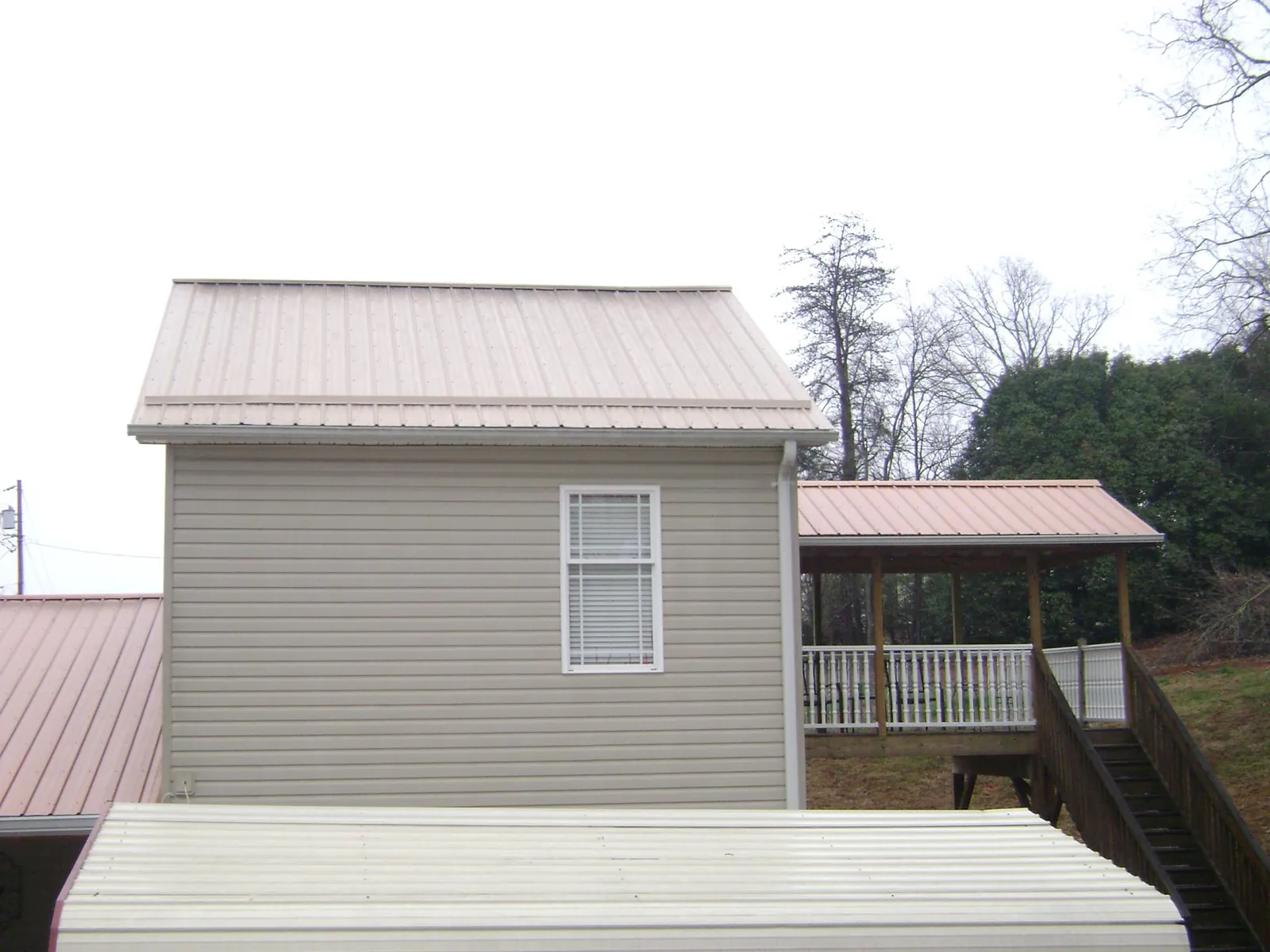 Tan metal roofs on a two story addition and attached porch, from a Roof Replacement job in Boykins